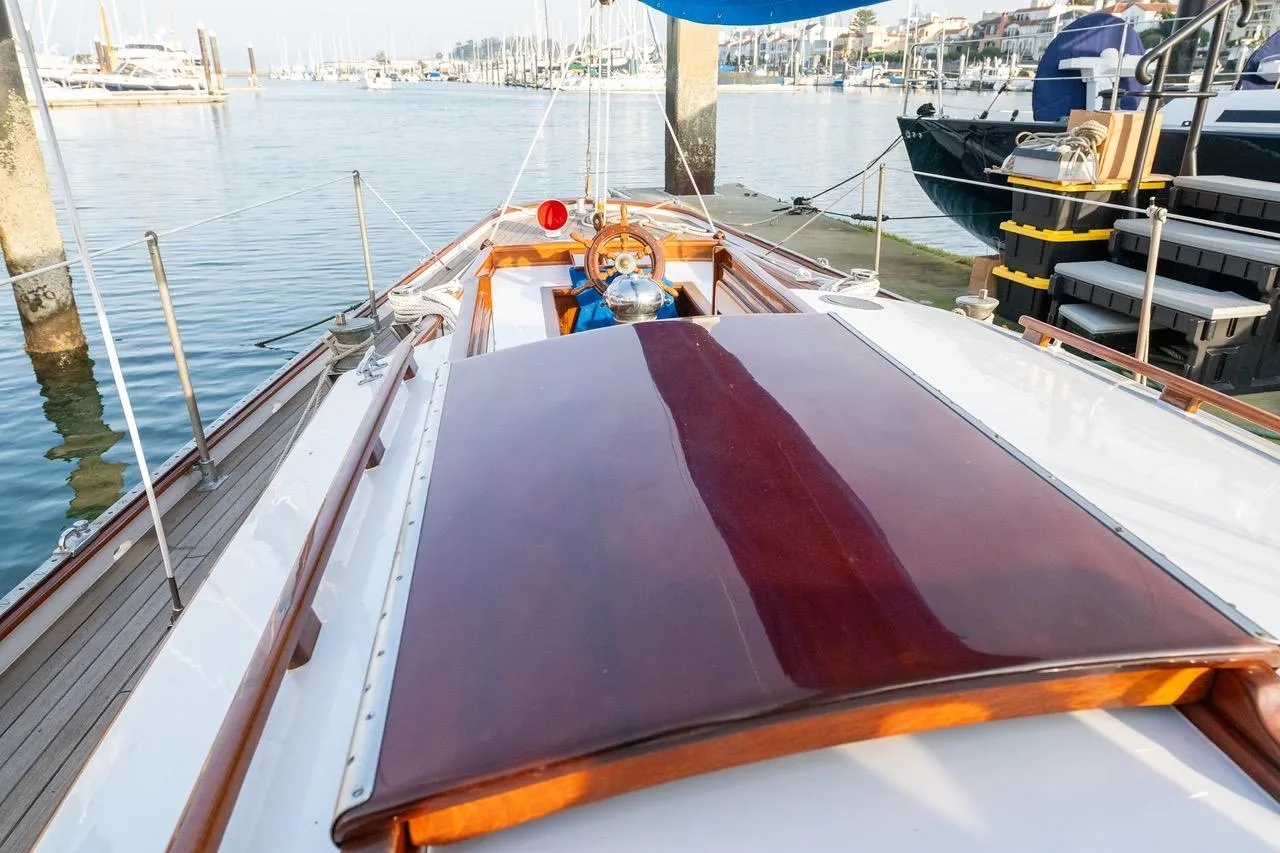 1938 Philip Rhodes Cutter sailboat with polished wood deck, docked in a marina.