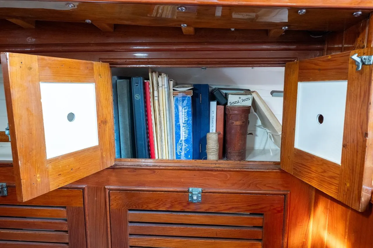 Wooden cabinet with open doors revealing books and nautical items inside.