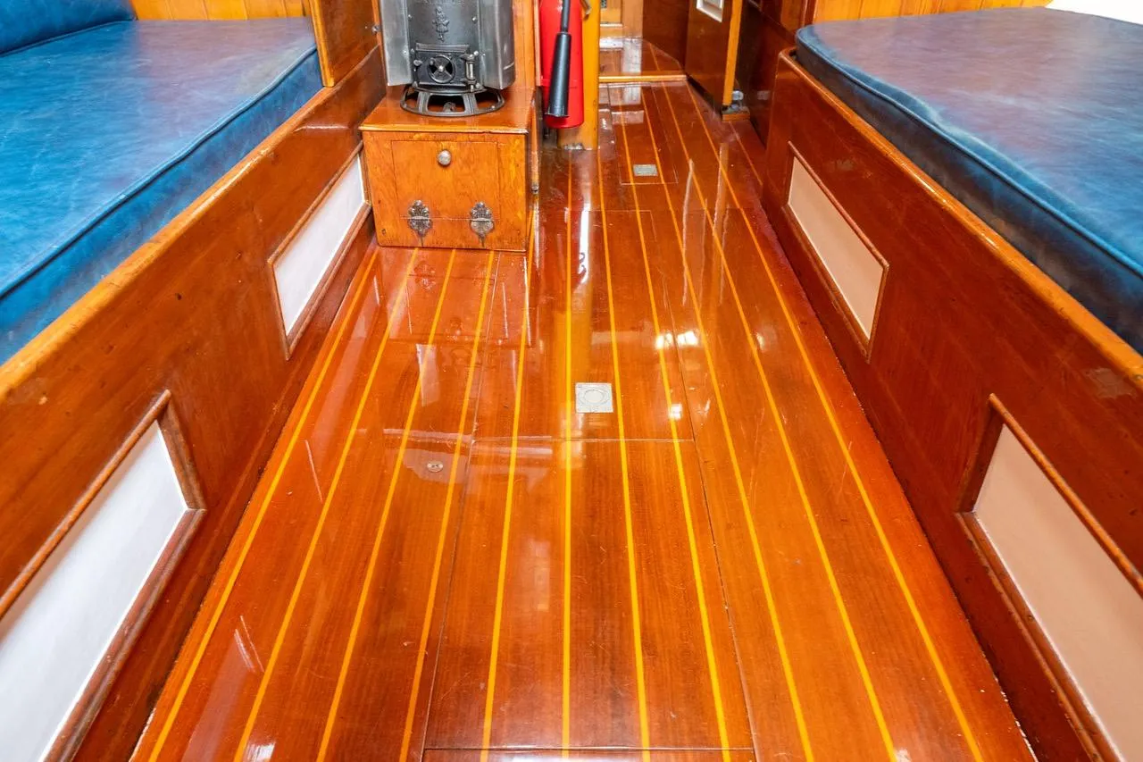 Polished wooden interior of 1938 Philip Rhodes Cutter boat, featuring blue cushioned seating.