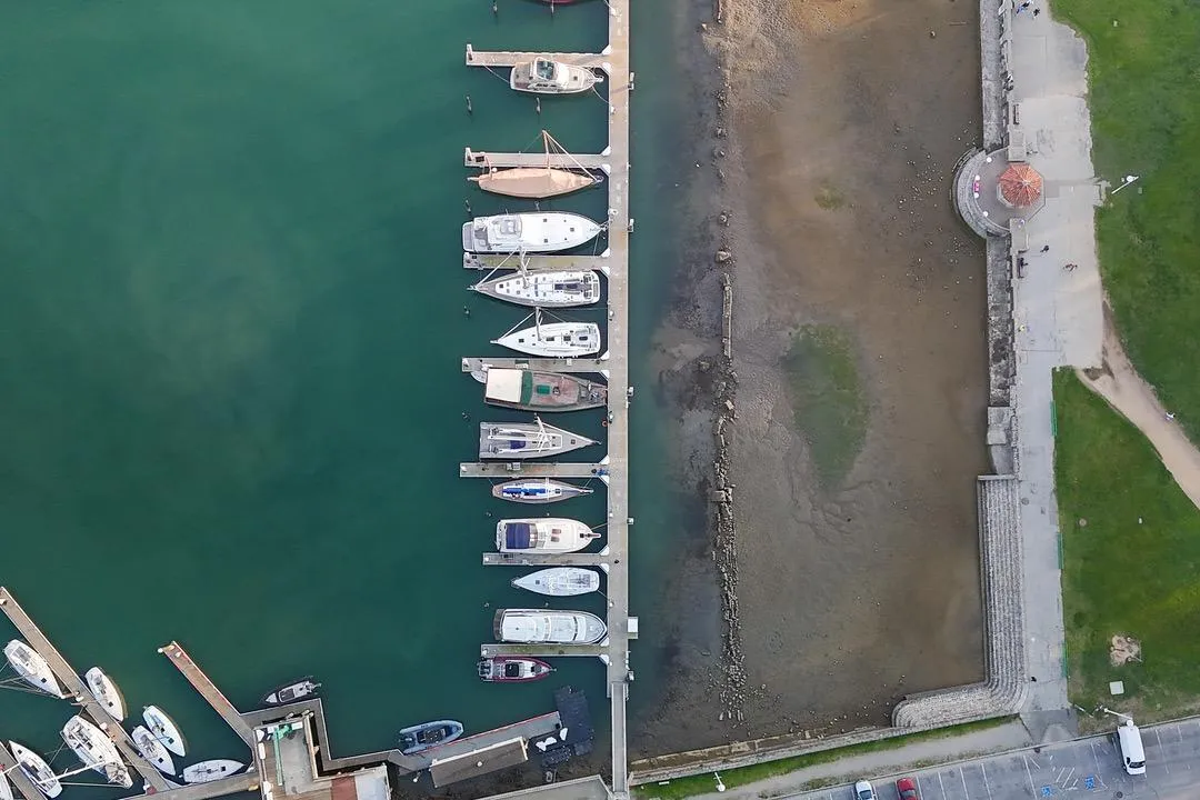 Aerial view of marina with boats, including a 1938 Philip Rhodes Cutter, docked alongside a promenade.