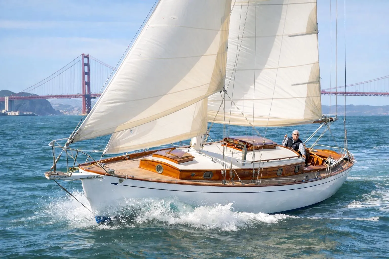 Vintage 1938 Rhodes Cutter sailboat cruising near Golden Gate Bridge.