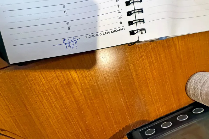 Legacy Yacht Photos Pics Open notebook on wooden table with handwritten contact number, spiral binding visible.