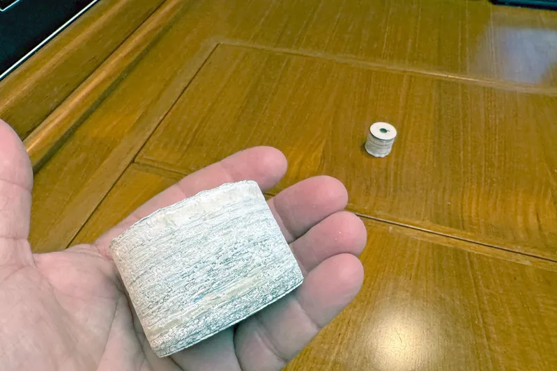 Legacy Yacht Photos Pics Hand holding a large, textured, cylindrical object on a wooden table, smaller cylinder in background.