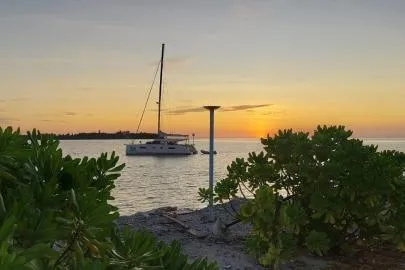 Kaikira Yacht Photos Pics 2019 Nautitech 46 catamaran anchored at sunset near a tropical shoreline.