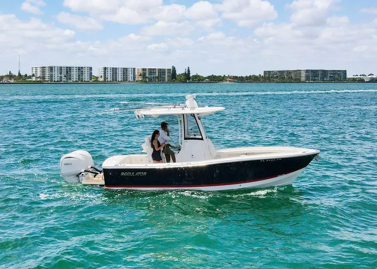  Yacht Photos Pics 2024 Regulator 23 boat cruising on clear blue water with cityscape background.