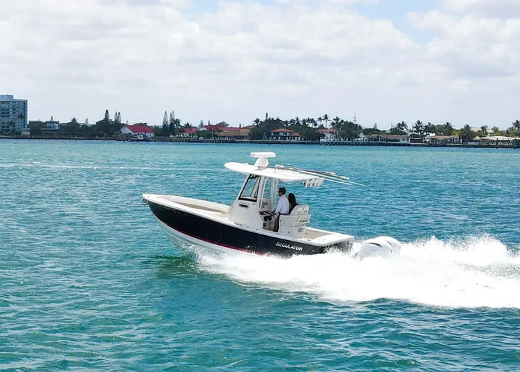  Yacht Photos Pics 2024 Regulator 23 boat cruising on blue water near a coastal town.