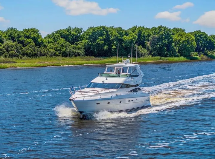 Vortex Yacht Photos Pics 2004 Neptunus 56 Flybridge yacht cruising on a scenic river with lush green trees.