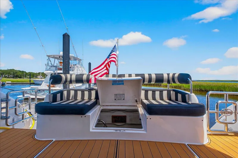 Vortex Yacht Photos Pics 2004 Neptunus 56 Flybridge yacht with striped seating and American flag, docked by serene waters.
