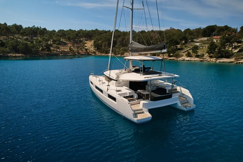 Spellbound Yacht Photos Pics 2023 Lagoon 50 catamaran sailing in clear blue waters near a forested coastline.