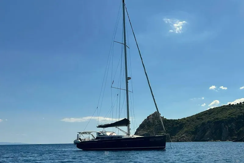 Boxter Yacht Photos Pics Sailing yacht Beneteau Sense 50 (2013) on serene blue waters near a rocky coastline.