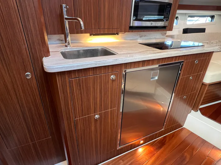 Yacht Photos Pics 2023 Pursuit OS 355 Offshore yacht kitchen with wood cabinetry, sink, and modern appliances.