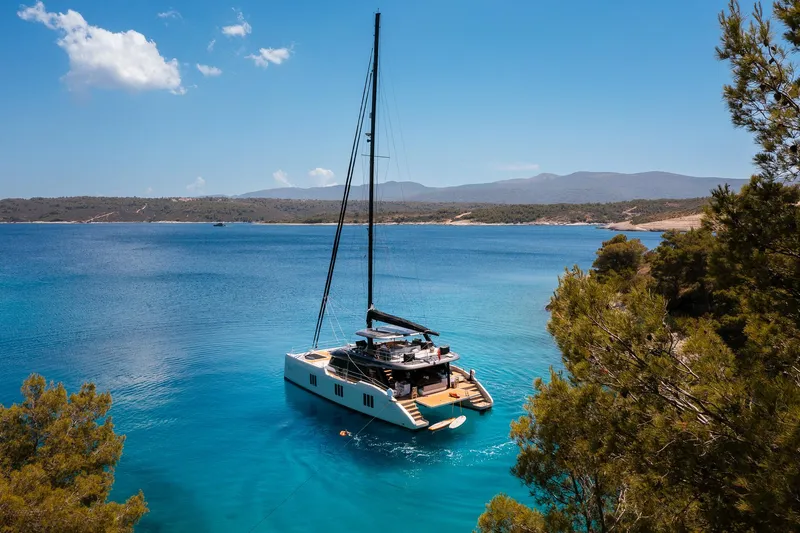 N+1 Yacht Photos Pics 2024 Sunreef 70 Eco yacht anchored in a serene, turquoise bay surrounded by lush greenery.
