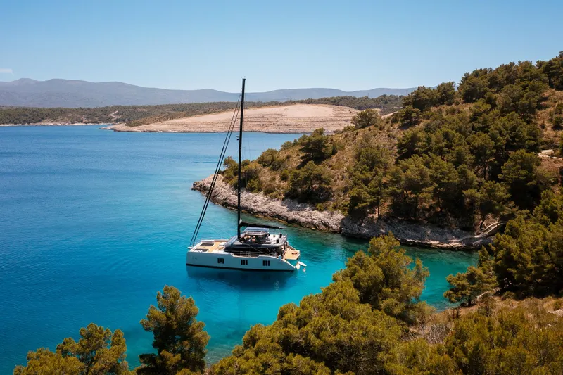 N+1 Yacht Photos Pics Luxurious 2024 Sunreef 70 Eco yacht anchored in a serene, turquoise bay surrounded by lush greenery.