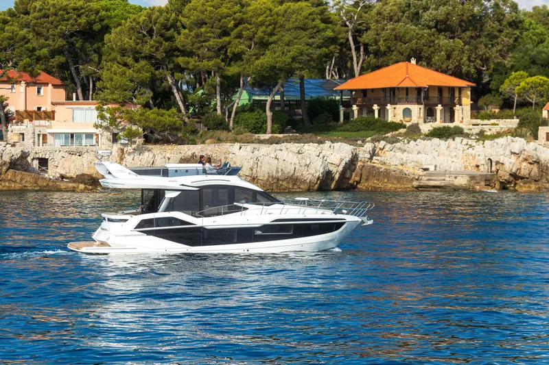  Yacht Photos Pics 2026 Galeon 480 Fly yacht cruising near coastal villas and lush greenery.