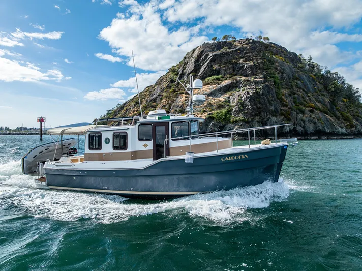 Caldonia Yacht Photos Pics 2013 Ranger Tugs R 29 cruising near a rocky island under a partly cloudy sky.
