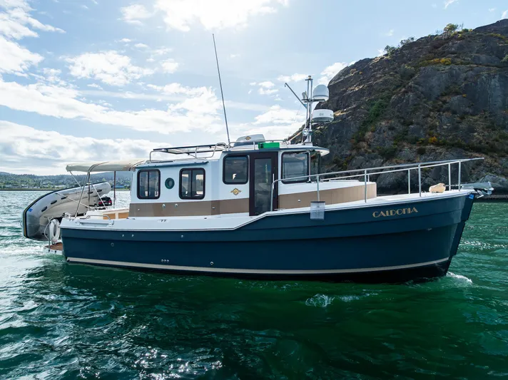 Caldonia Yacht Photos Pics 2013 Ranger Tugs R 29 boat on water, near rocky shoreline under blue sky.