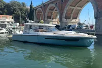 2023 Nimbus W11 boat docked near a stone arch bridge on a sunny day.