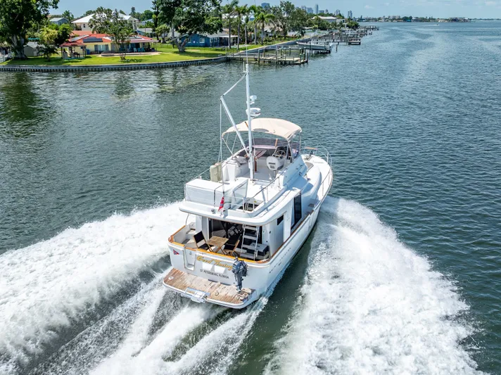 Good Timimg Yacht Photos Pics 2015 Beneteau Swift Trawler 34 cruising on a scenic waterway, surrounded by lush greenery.
