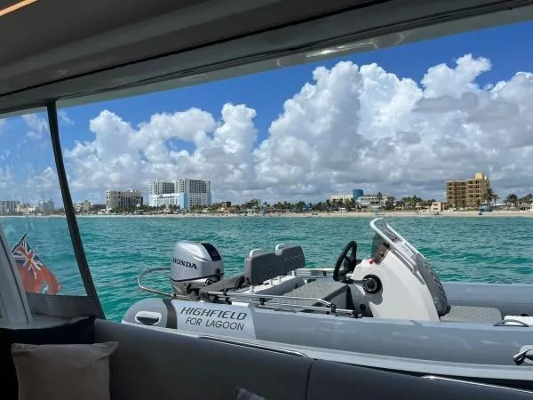 Sunlove Yacht Photos Pics 2024 Lagoon SIXTY 7 yacht with tender, coastal cityscape view, clear skies, and turquoise waters.