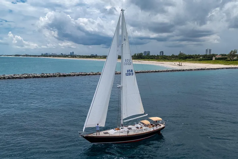 Ghost Yacht Photos Pics Hinckley Sou'wester Stoway Sloop 2000 sailing near a scenic coastline under cloudy skies.