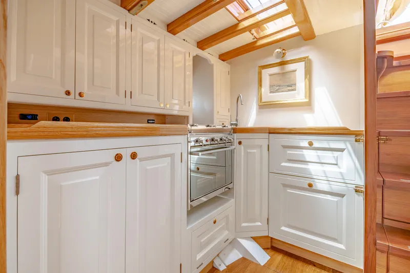 Armide Yacht Photos Pics 1938 Custom Classic Works kitchen with white cabinetry, wooden accents, and natural light.