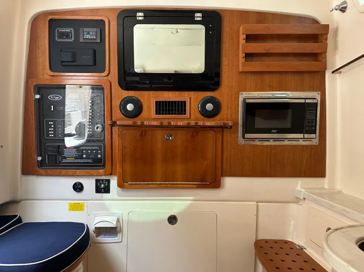  Yacht Photos Pics 2023 Grady-White Canyon 376 cabin interior with control panel, microwave, and wooden cabinetry.