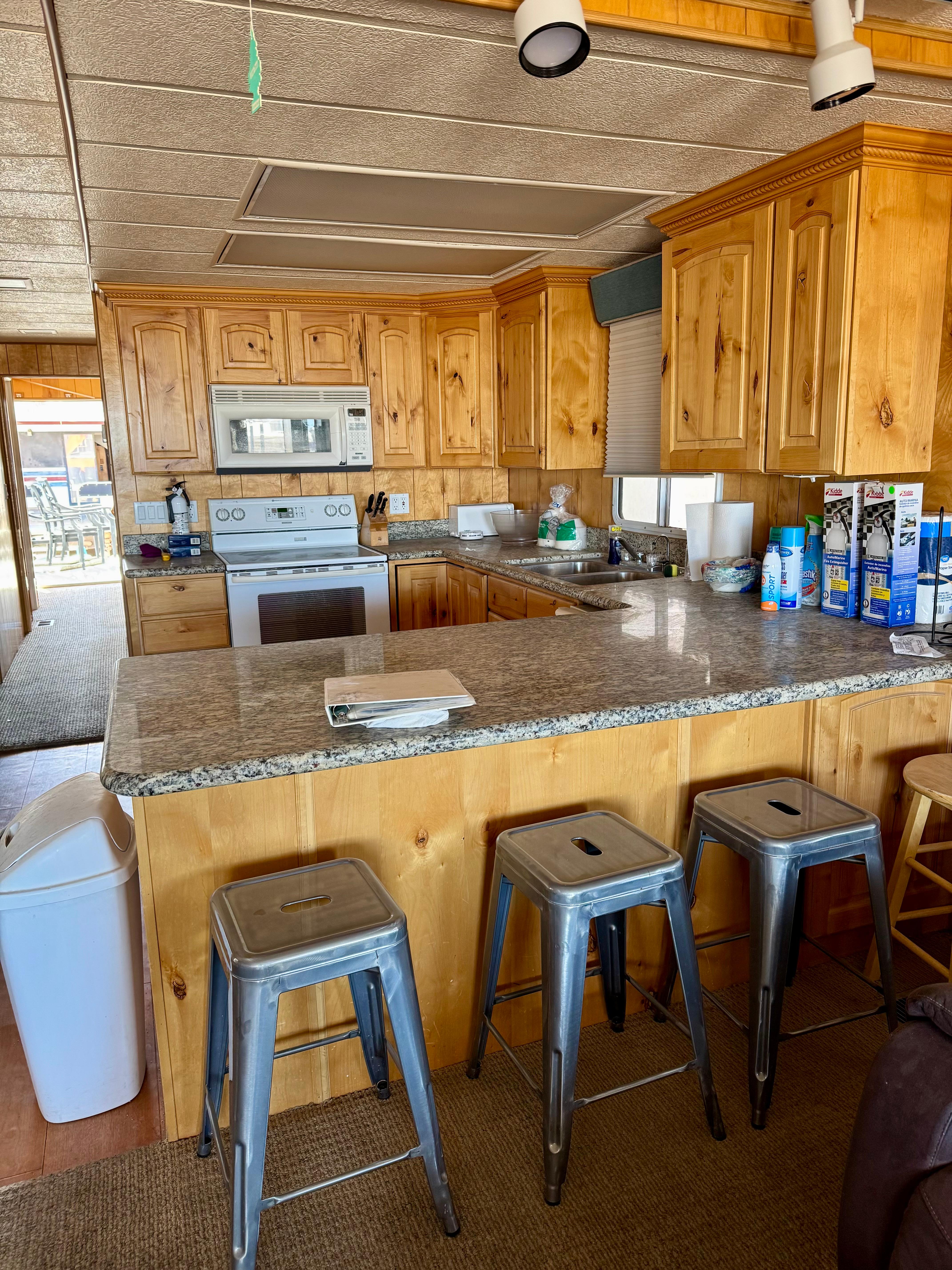 Rustic kitchen with wooden cabinets, granite countertops, and metal stools in a 1993 Lakeview model.