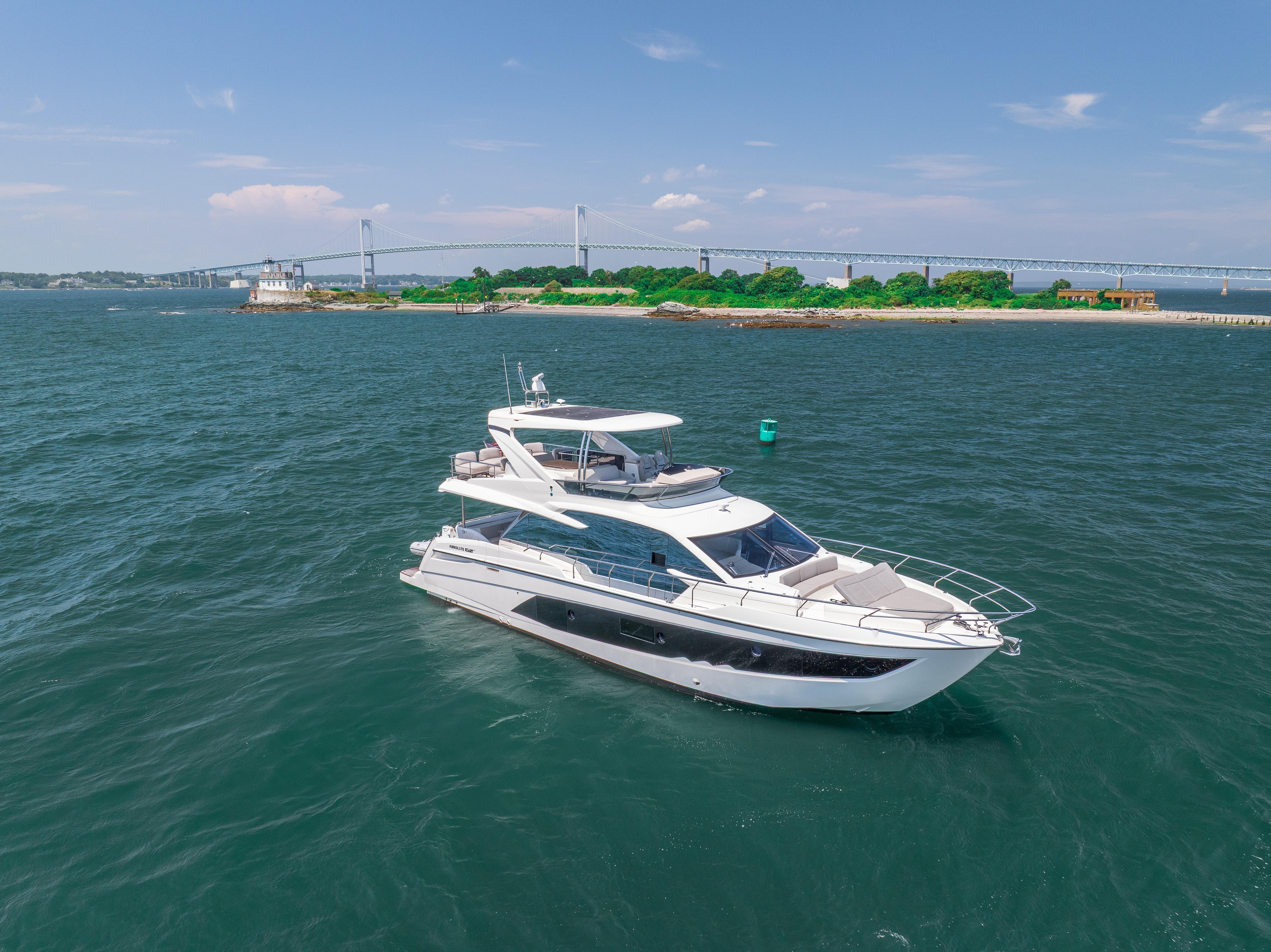 2023 Absolute 62 Fly yacht cruising near a scenic coastline with a bridge in the background.