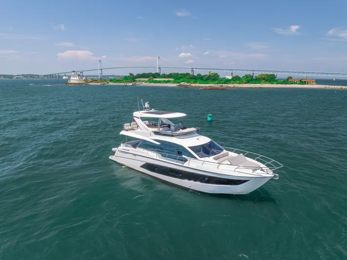  Yacht Photos Pics 2023 Absolute 62 Fly yacht cruising near a scenic coastline with a bridge in the background.