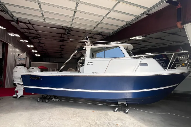  Yacht Photos Pics 2026 Parker 2520 XLD Sport Cabin boat in a showroom, featuring a sleek blue and white design.