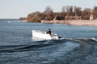2024 Rand Picnic 18 boat cruising on a serene lake near a picturesque shoreline.