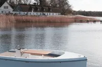 2024 Rand Picnic 18 boat on serene lake near rustic houses and trees.