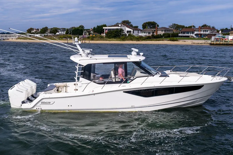  Yacht Photos Pics 2024 Boston Whaler 405 Conquest cruising on water near coastal homes.