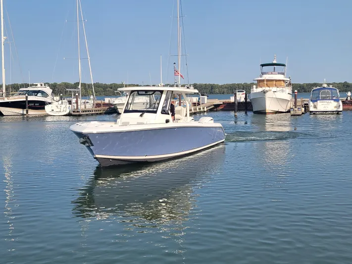 Over Bohr’d Yacht Photos Pics 2023 Pursuit S 328 Sport boat cruising in a marina with other vessels.