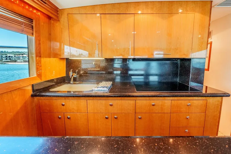 Reel Ranchin Yacht Photos Pics Luxurious kitchen interior of 2004 Hatteras 54 Convertible yacht with wood cabinetry and black countertops.