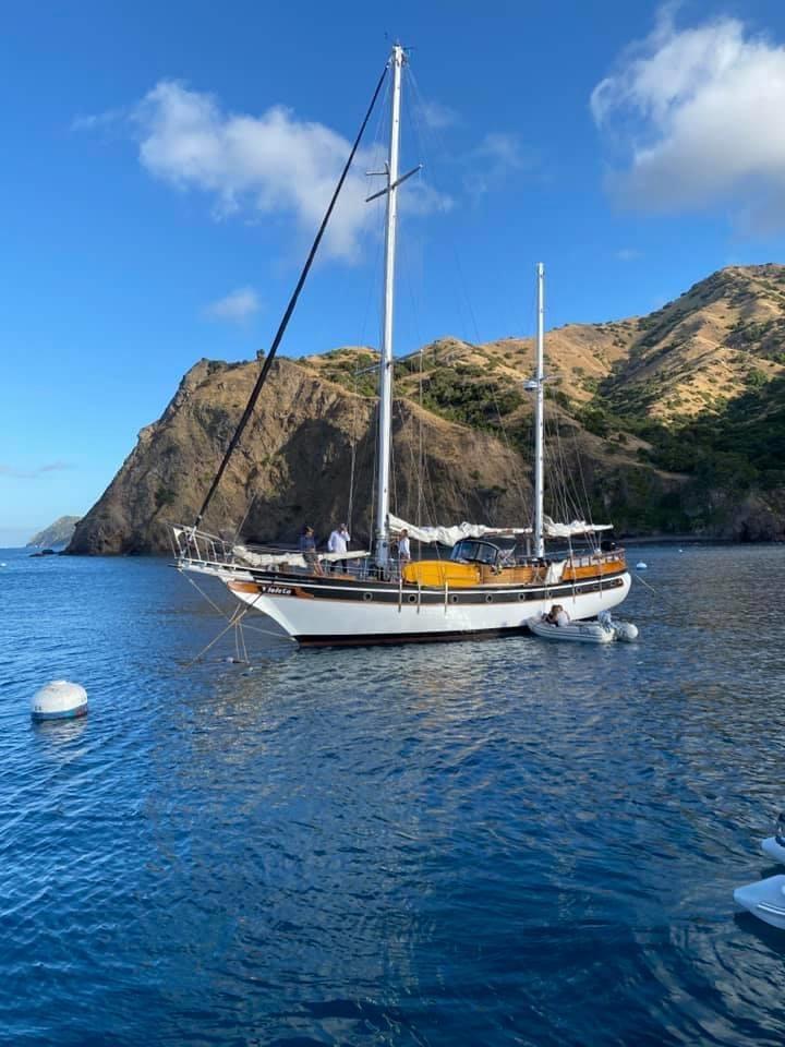 Sailboat Formosa 51, 1975 model, anchored near rocky coastline under blue sky.