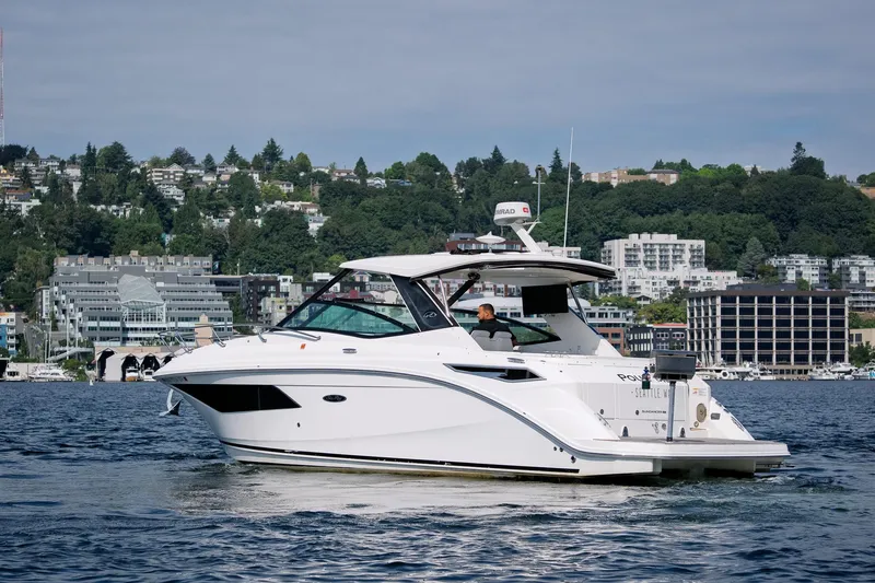  Yacht Photos Pics 2019 Sea Ray Sundancer 320 cruising on a scenic waterfront with urban backdrop.