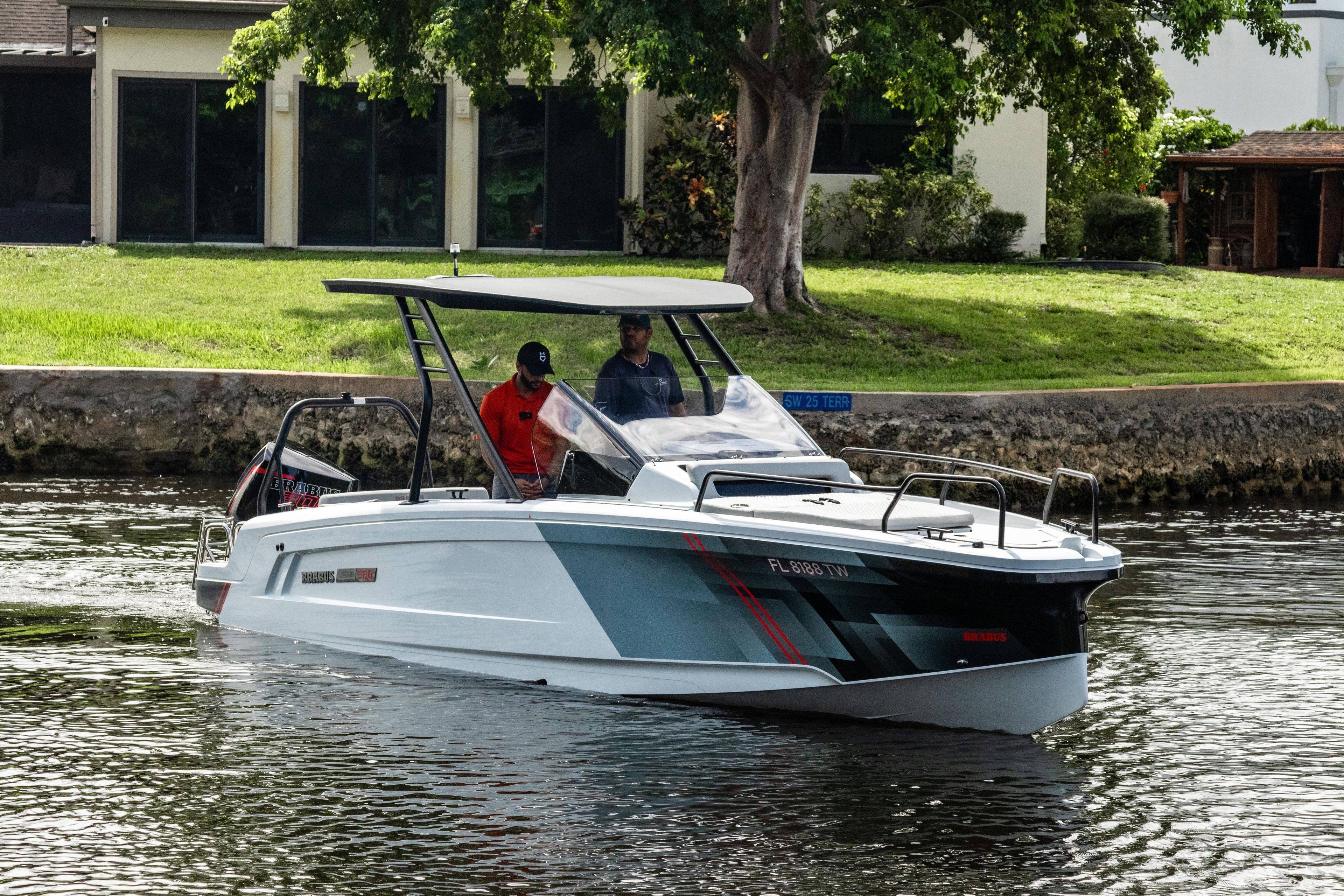 2023 BRABUS Shadow 300 XT boat cruising on a calm waterway near a grassy shoreline.