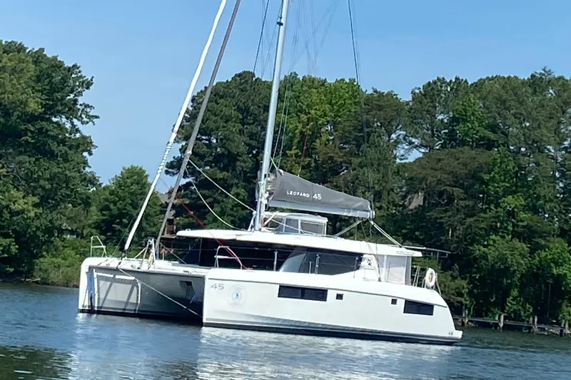 Why Knot Yacht Photos Pics 2020 Robertson Leopard catamaran sailing on a calm lake with lush green trees.