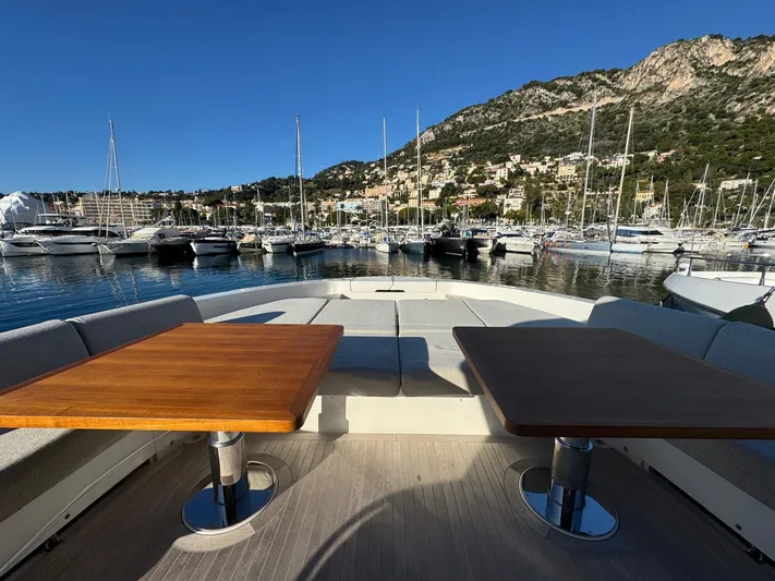  Yacht Photos Pics 2022 Bluegame BGX70 yacht deck with wooden tables, overlooking marina and scenic hillside.