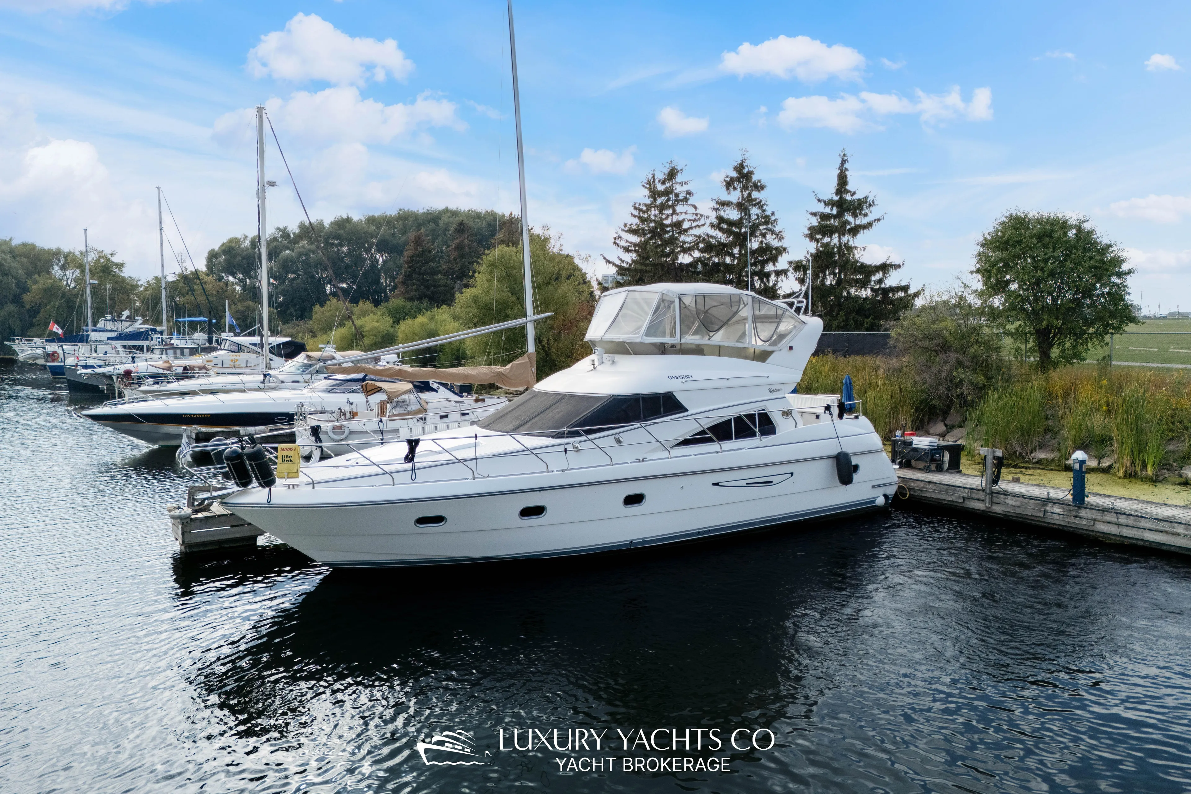  Yacht Photos Pics 1997 Neptunus 50 Aft Cabin yacht docked at marina, surrounded by lush greenery.