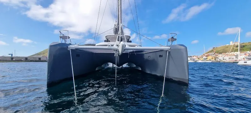 Kajikia Yacht Photos Pics Front view of 2023 Lagoon 77 catamaran on water under blue sky.