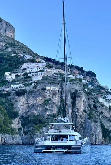 Kajikia Yacht Photos Pics 2023 Lagoon 77 yacht sailing near scenic coastal cliffs and hillside village.