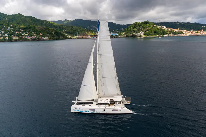 Inky Blue Yacht Photos Pics 2020 Outremer 51 catamaran sailing near lush, green coastline under cloudy skies.