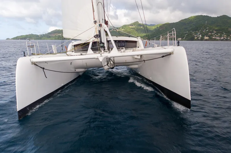Inky Blue Yacht Photos Pics 2020 Outremer 51 catamaran sailing on open sea with lush green hills in background.