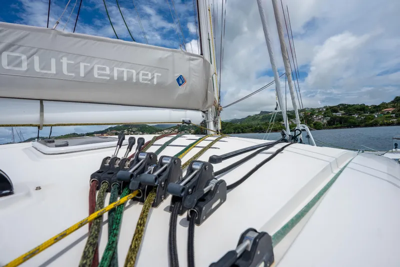Inky Blue Yacht Photos Pics 2020 Outremer 51 sailboat deck with rigging, sailing near lush coastline under cloudy skies.