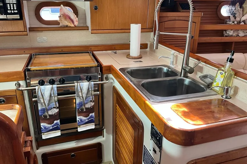 Spellbound Yacht Photos Pics Interior of 2000 Catalina 470 yacht kitchen with stove, sink, and wooden cabinetry.