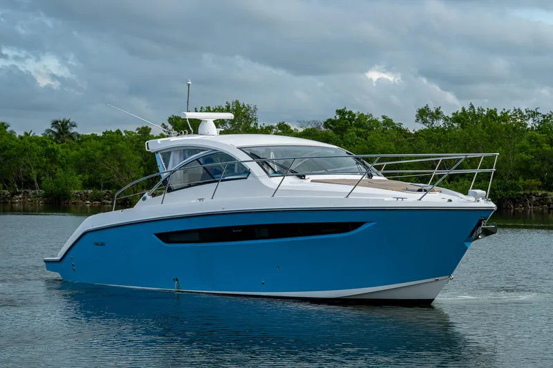  Yacht Photos Pics 2018 Pursuit SC 365i Sport Coupe boat on calm water, surrounded by lush greenery.