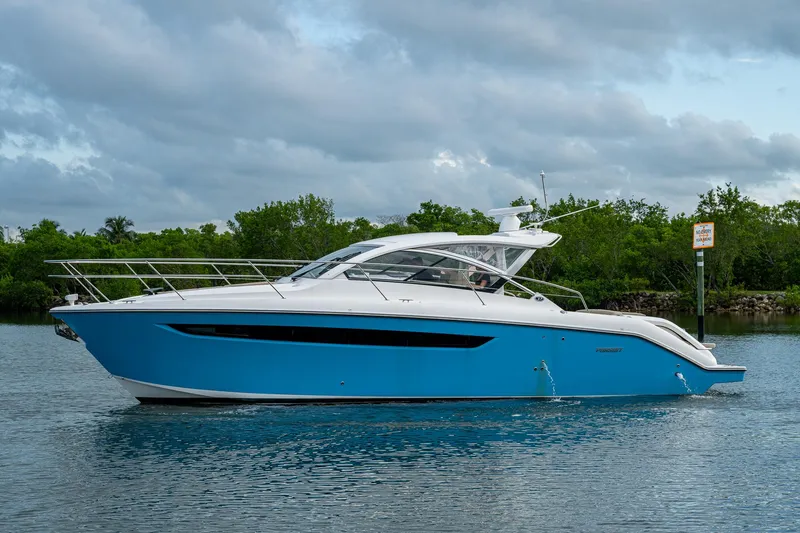  Yacht Photos Pics 2018 Pursuit SC 365i Sport Coupe boat on calm water, surrounded by lush greenery.