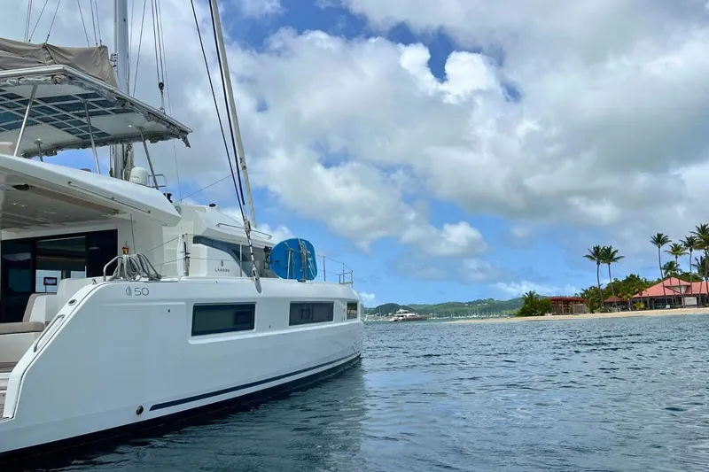 Dignity Yacht Photos Pics 2021 Lagoon 50 catamaran sailing near tropical island with palm trees and blue sky.